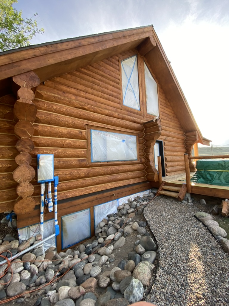 Log home staining in progress with windows masked for protection